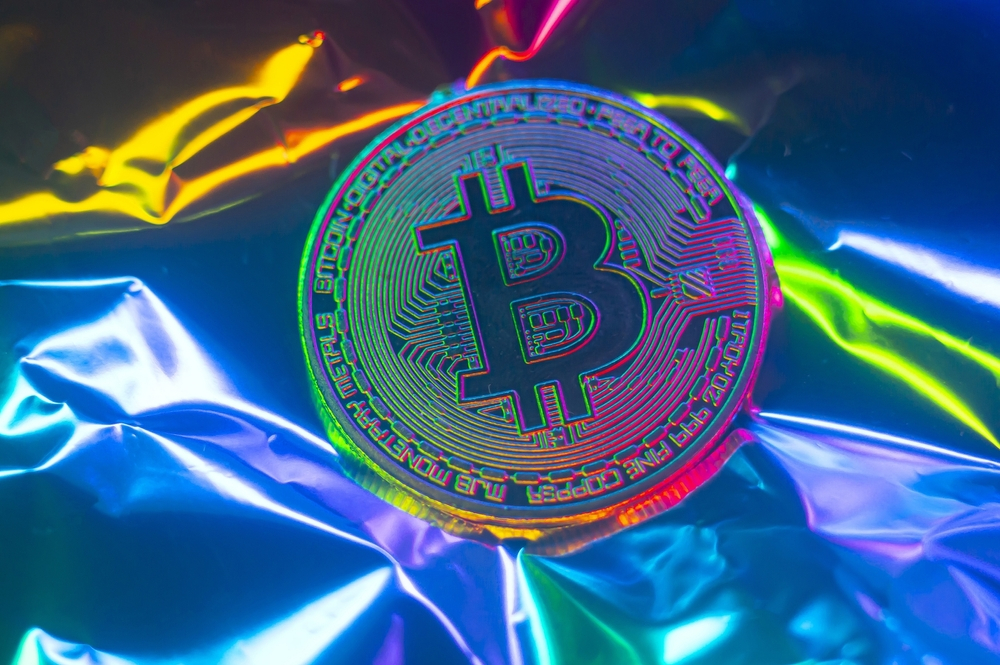 A Bitcoin coin cast in iridescent hues against a reflective surface, creating a vibrant and colorful display that signifies the modern and digital nature of cryptocurrency in today's economy.