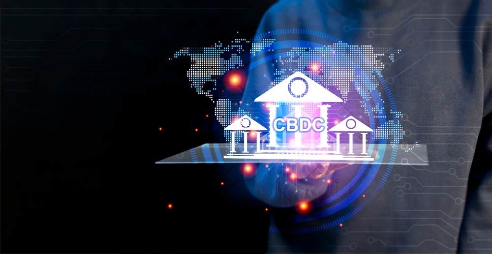An image illustrating the concept of Central Bank Digital Currencies (CBDC), featuring a graphic of a bank with the acronym CBDC projected over a digital tablet held by a person. The backdrop includes a dotted world map, implying the global impact of digital currencies issued by central banks. The futuristic design elements suggest innovation in the financial sector.