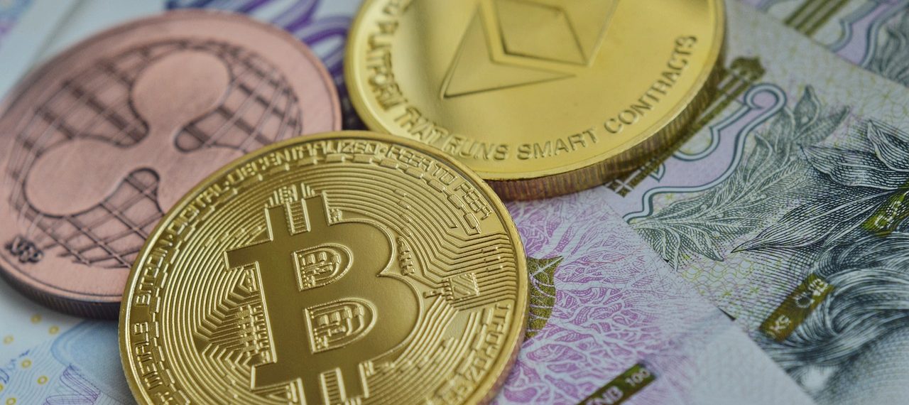 A photo showcasing three cryptocurrency coins on top of a banknote. The coins feature the logos of Bitcoin, Ripple (XRP), and Ethereum, indicating their respective digital currencies. The image highlights the intersection of traditional and digital finance.
